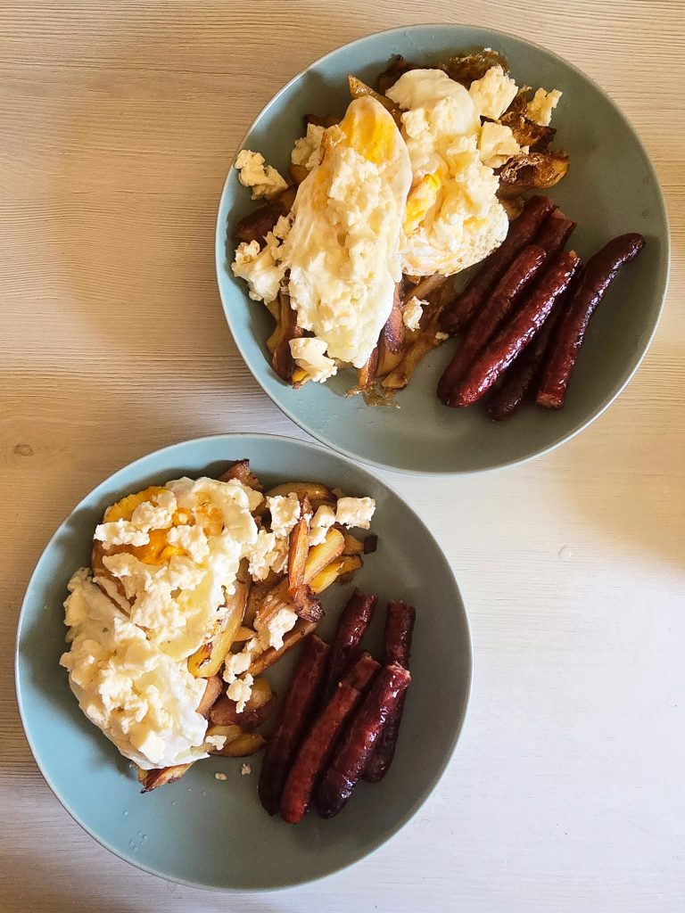 Two plates of comfort food: potatoes, fried eggs, sausages