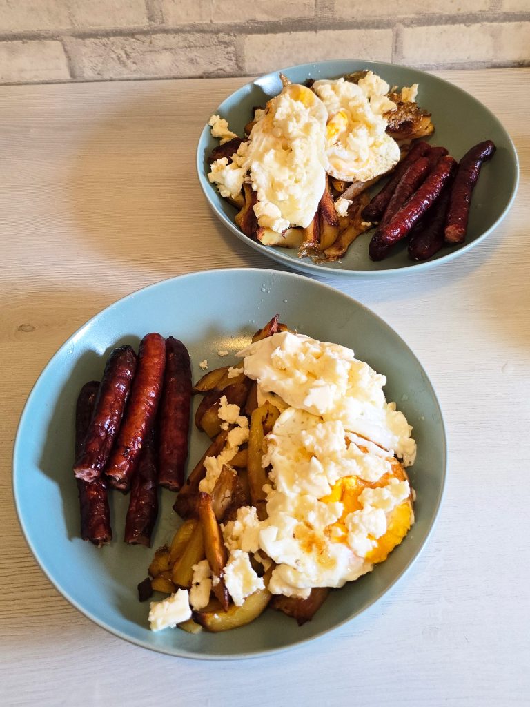 Two plates of comfort food: potatoes, fried eggs, sausages